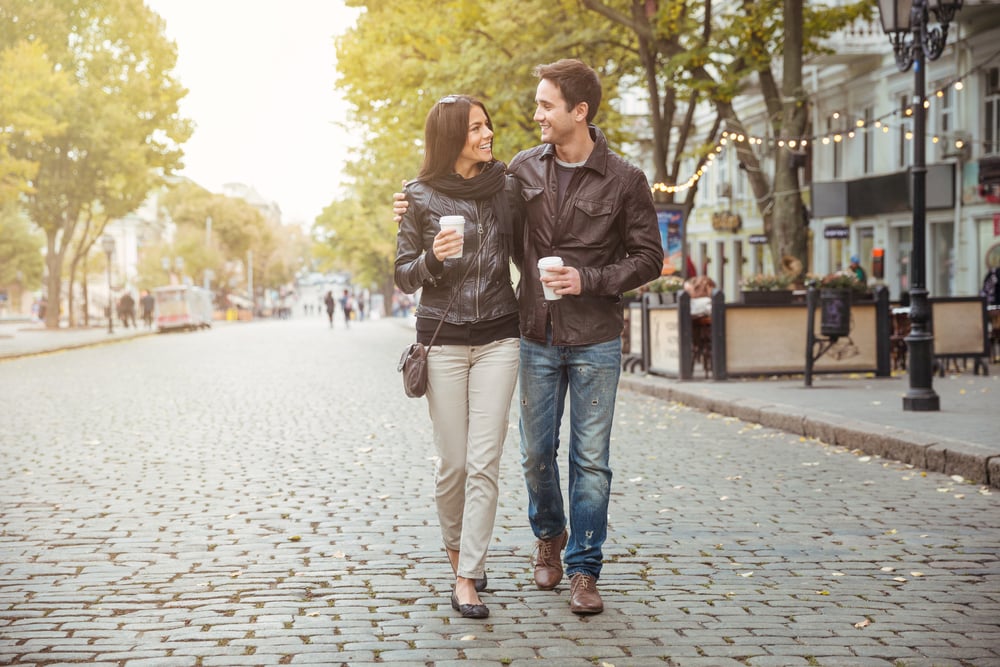 Portrait of a happy romantic couple with coffee walking outdoors in old european city